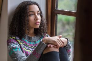 teen sitting against wall looking pensive while struggling with symptoms of depression