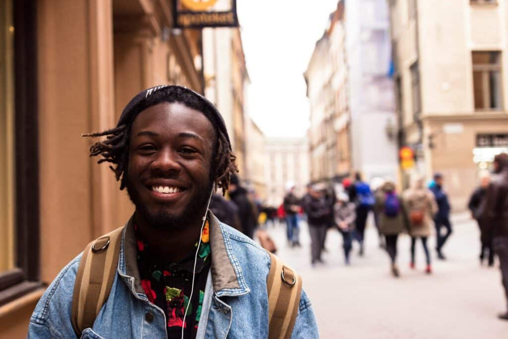 young man smiling wearing denim shirt and a beanie, wired earbuds in