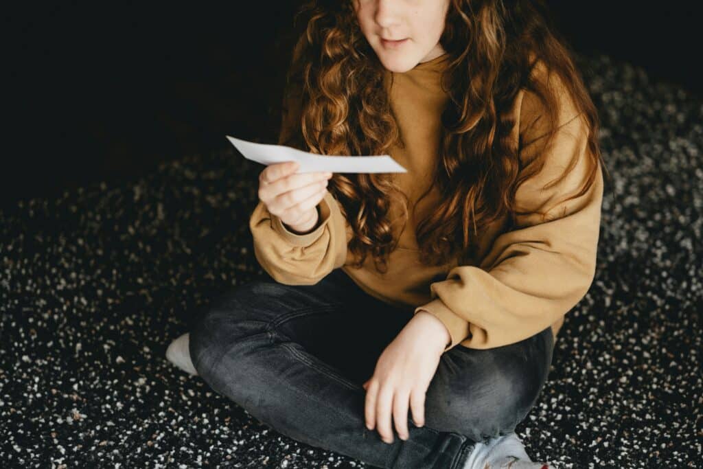 teen girl sitting cross-legged on the floor reading a slip of paper