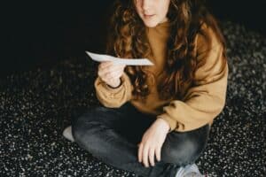 teen girl sitting cross-legged on the floor reading a slip of paper